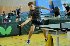Mann spielt Tischtennis an einer Tischtennisplatte in einer Sporthalle.