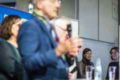 Mehrere Personen auf einer Konferenz, eine Person spricht vorne ins Mikrofon.