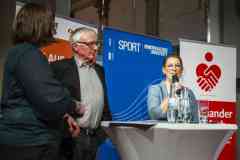 Drei Personen bei einer Podiumsdiskussion vor Sport- und Hochschul-Bannern, eine Frau spricht am Stehtisch ins Mikrofon.