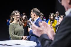 Mann mit Mikrofon interviewt eine Frau bei einer Veranstaltung, während das Publikum applaudiert.
