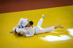 Zwei Judoka in weißen Anzügen ringen auf einer gelben Matte.