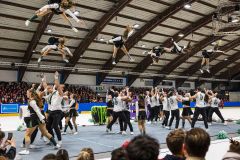 Akrobatische Tanzgruppe bei einer Turnshow in einer Eishalle, mit mehreren Springerinnen in der Luft und Publikum im Hintergrund.