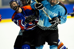 Drei Eishockeyspieler in Helmen und Trikots kämpfen um den Puck auf dem Eis.