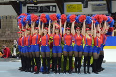 Cheerleader-Gruppe in roter und blauer Kleidung mit Pompons in einer Halle.