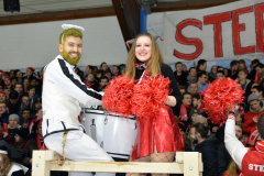 Kostümierte Personen mit Trommel und roten Pompons vor einer Menschenmenge in einer Halle.