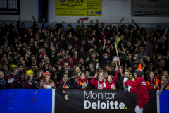 Große Menschenmenge hinter einer Absperrung, mit erhobenen Armen; vorne ein Banner mit „Monitor Deloitte“.