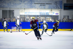 Eishockeyspieler auf dem Eis vor einem Tor, mit Bande und Zuschauerbereich im Hintergrund.