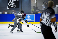 Zwei Eishockeyspieler kämpfen um den Puck, ein Schiedsrichter steht unscharf im Vordergrund.