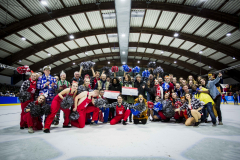 Gruppe von Personen auf einer Eisfläche in einer Halle, einige halten Pompons und ein großes Scheck-Schild.