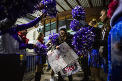 Gruppe mit violetten Pompons hält bemalte Schilder in einer Halle.