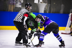 Schiedsrichter und zwei Eishockeyspieler beim Bully vor dem Tor auf dem Eis.
