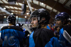Eishockeyspieler in blauen und schwarzen Trikots mit Helmen in einer Halle, zwei Gesichter sind verdeckt.
