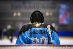 Eishockeyspieler von hinten mit blauem Trikot, Helm und Schläger auf dem Eis.