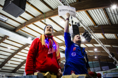 Zwei Personen in roter und blauer Kleidung, die rechte hält ein Schild mit „STEELERS“ hoch.