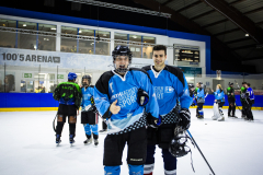 Eishockeyspieler in blauen Trikots auf dem Eis in einer Halle, im Hintergrund weitere Spieler und Bande.