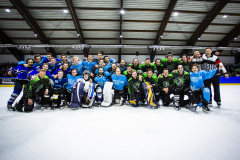Eishockeymannschaft in farbigen Trikots posiert kniend auf dem Eis in einer Halle.