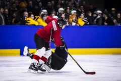 Eishockeyspieler in rotem Trikot und schwarzer Ausrüstung auf dem Eis, Gegner in Schwarz stürzt daneben.
