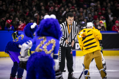 Eishockey-Anspiel mit Schiedsrichter, zwei Spielern in blauen Kostümen und einem Spieler in gelbem Kostüm auf dem Eis.