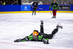 Eishockeyspieler liegt auf dem Eis; zwei weitere Spieler stehen im Hintergrund.