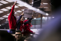 Personen in roten Kleidern in einer Halle, eine hält ein Schild mit der Aufschrift „STEELERS“.