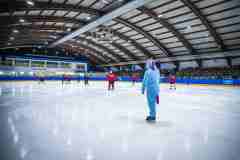 Eishockeyspiel in einer Halle, im Vordergrund eine Person im blauen Einhornkostüm auf dem Eis.