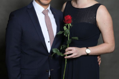 Mann im dunklen Anzug und Frau im langen dunklen Kleid, sie hält eine rote Rose.