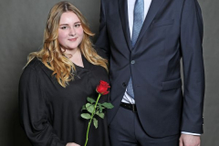 Frau und Mann stehen nebeneinander vor grauem Hintergrund; die Frau hält eine rote Rose.