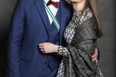 Mann im blauen Anzug und Frau im gemusterten Kleid stehen eng nebeneinander vor grauem Hintergrund.