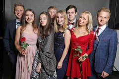 Sechs festlich gekleidete Personen stehen nebeneinander; zwei Frauen halten rote Rosen.