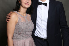 Zwei Personen stehen vor grauem Hintergrund; er trägt Anzug und Fliege, sie ein rosafarbenes Abendkleid.