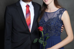 Mann im dunklen Anzug mit roter Krawatte und Frau im blauen Kleid; sie hält eine rote Rose.