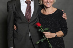 Mann im Anzug und Frau im schwarzen Kleid stehen nebeneinander; die Frau hält eine rote Rose.