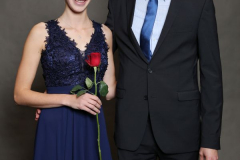 Frau im blauen Kleid mit roter Rose neben Mann im schwarzen Anzug.