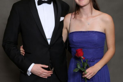 Mann im schwarzen Anzug und Frau im blauen Abendkleid, beide mit verdecktem Gesicht; sie hält eine rote Rose.