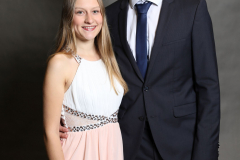 Mann im dunklen Anzug und Frau im hellen Kleid stehen vor grauem Hintergrund.