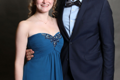 Ein Mann im dunkelblauen Anzug und eine Frau im blauen Abendkleid stehen vor grauem Hintergrund.