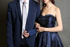 Ein Mann im dunkelblauen Anzug und eine Frau im dunkelblauen trägerlosen Kleid stehen nebeneinander.