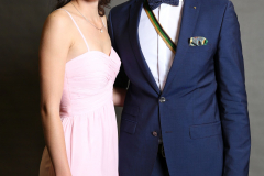 Eine Frau im rosa Abendkleid und ein Mann im blauen Anzug stehen vor grauem Hintergrund.