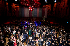 Großer Ballsaal mit tanzenden Menschen in Abendkleidung und einem Cluster roter Ballons an der Decke.