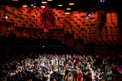 Tanzende Paare in einem Saal mit roter Ballondekoration, Holzfußboden und vielen runden Deckenleuchten.