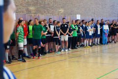 Gruppe von Sportlern in Trikots steht nebeneinander an einer Hallenwand in einer Sporthalle.