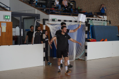 Mehrere Personen in einer Sporthalle vor einem Tor; eine Person hält ein weißes Schild hoch.