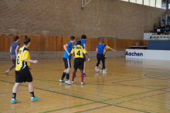 Mehrere Personen spielen in einer Sporthalle Hallenfußball; im Hintergrund steht „Aachen“.