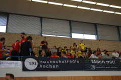 Zuschauer auf einer Tribüne in einer Halle; Banner mit „Hochschulradio Aachen 99.1“ und „Mach mit!“