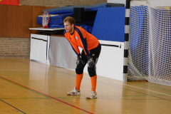 Torwart in orange-schwarzer Kleidung steht in einer Sporthalle vor dem Handballtor.