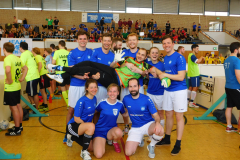 Gruppe von Sportlern in blauen und gelben Trikots in einer Halle, einige posieren, einer wird getragen.