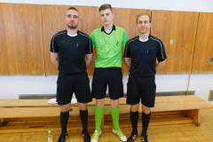 Drei Männer in Sportkleidung stehen vor Holzschränken in einer Umkleide.