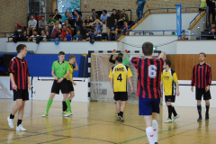 Hallensporthalle mit Handballspielern vor dem Tor, Zuschauer auf der Tribüne.