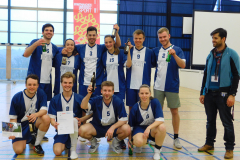 Elf Personen in blauen Sporttrikots in einer Halle, einige halten Flaschen und ein Blatt Papier.