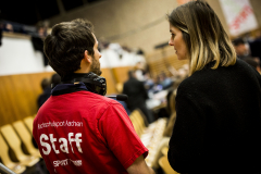 Person in rotem T-Shirt mit der Aufschrift „Hochschulsport Aachen Staff“ neben einer Frau in schwarzer Jacke.